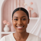 Close-up portrait of a smiling Black woman with sleek hair, looking confidently at the viewer. The background is blurred with