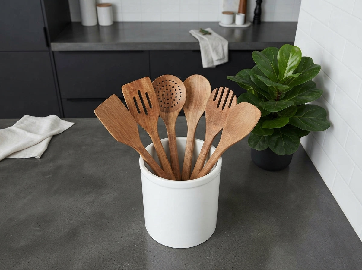 A 6-piece acacia wood utensil set in a white crock on a charcoal countertop in a modern, minimalist kitchen.
